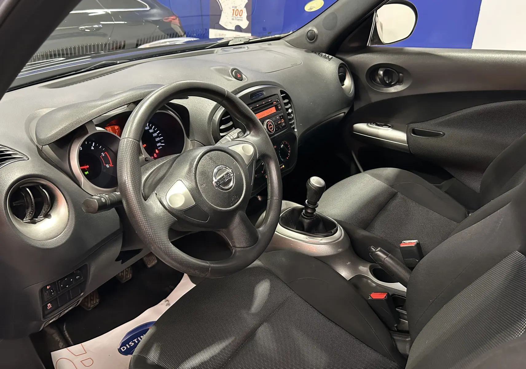 Vue intérieure côté conducteur du Nissan Juke noir métal 2012, volant cuir, tableau de bord et levier de vitesse manuel visibles.