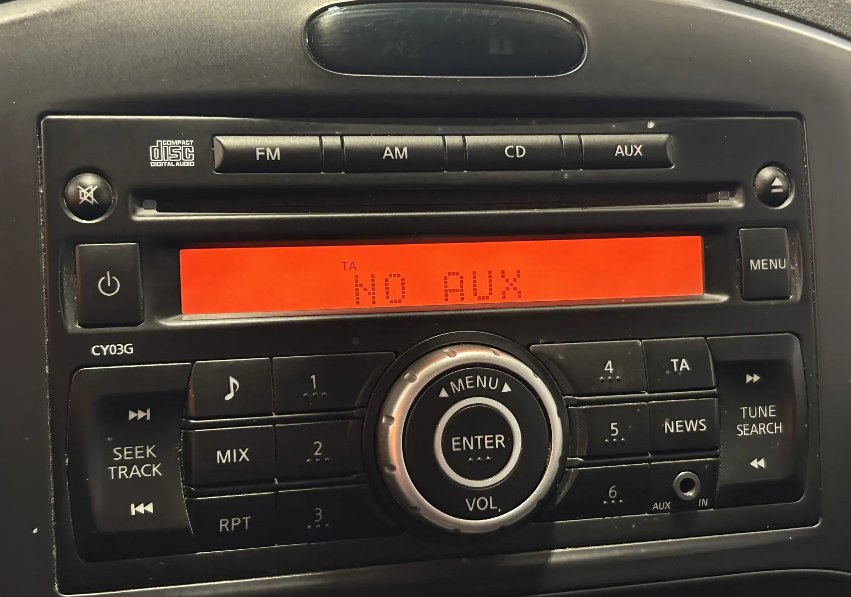 Gros plan sur la radio d’origine du Nissan Juke 2012 avec écran orange affichant "NO AUX" et boutons noirs.