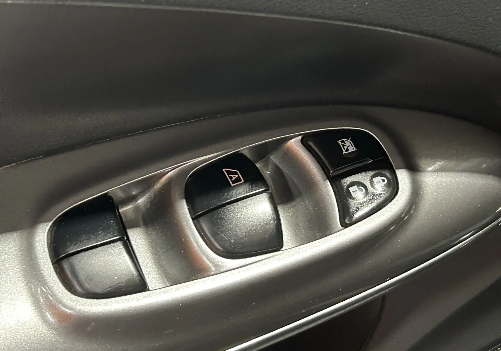 Gros plan sur les commandes de lève-vitres et verrouillage sur la portière côté conducteur du Nissan Juke noir métal.