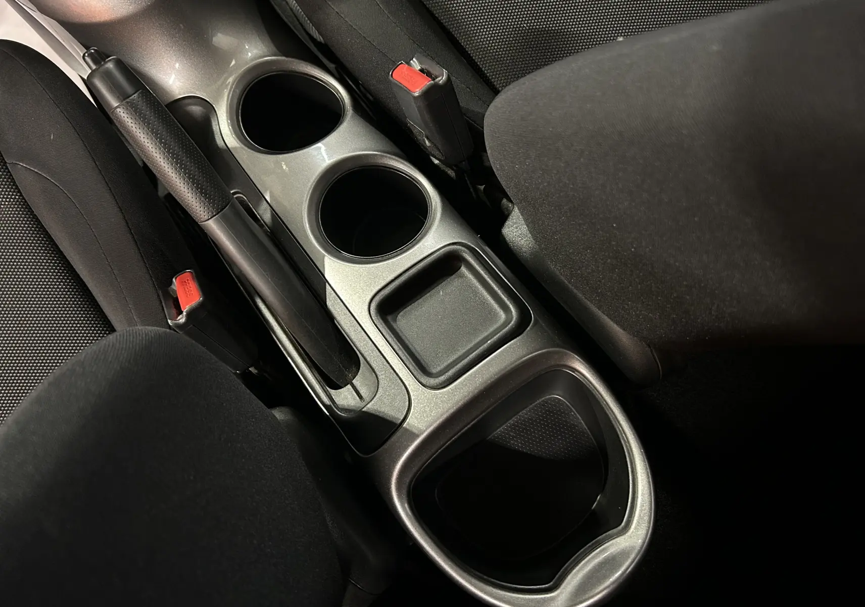 Vue rapprochée de la console centrale noire du Nissan Juke dci 110 Acenta, avec frein à main et porte-gobelets.