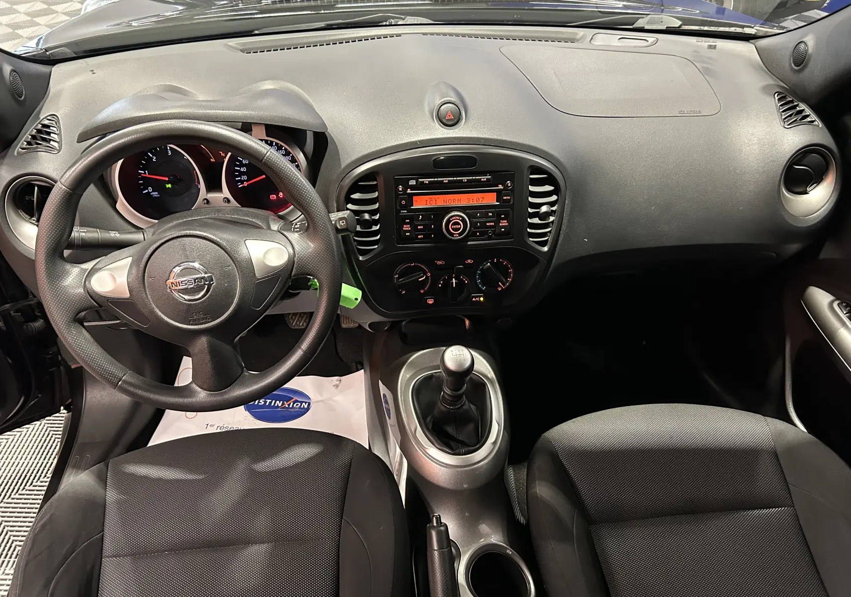 Vue intérieure frontale du tableau de bord et volant noir du Nissan Juke dci 110 Acenta avec boîte manuelle et sièges tissu noirs.