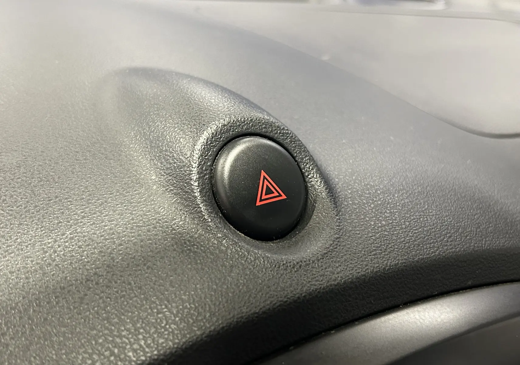 Gros plan sur le bouton de warning noir avec symbole rouge sur le tableau de bord d’un Nissan Juke noir métal.