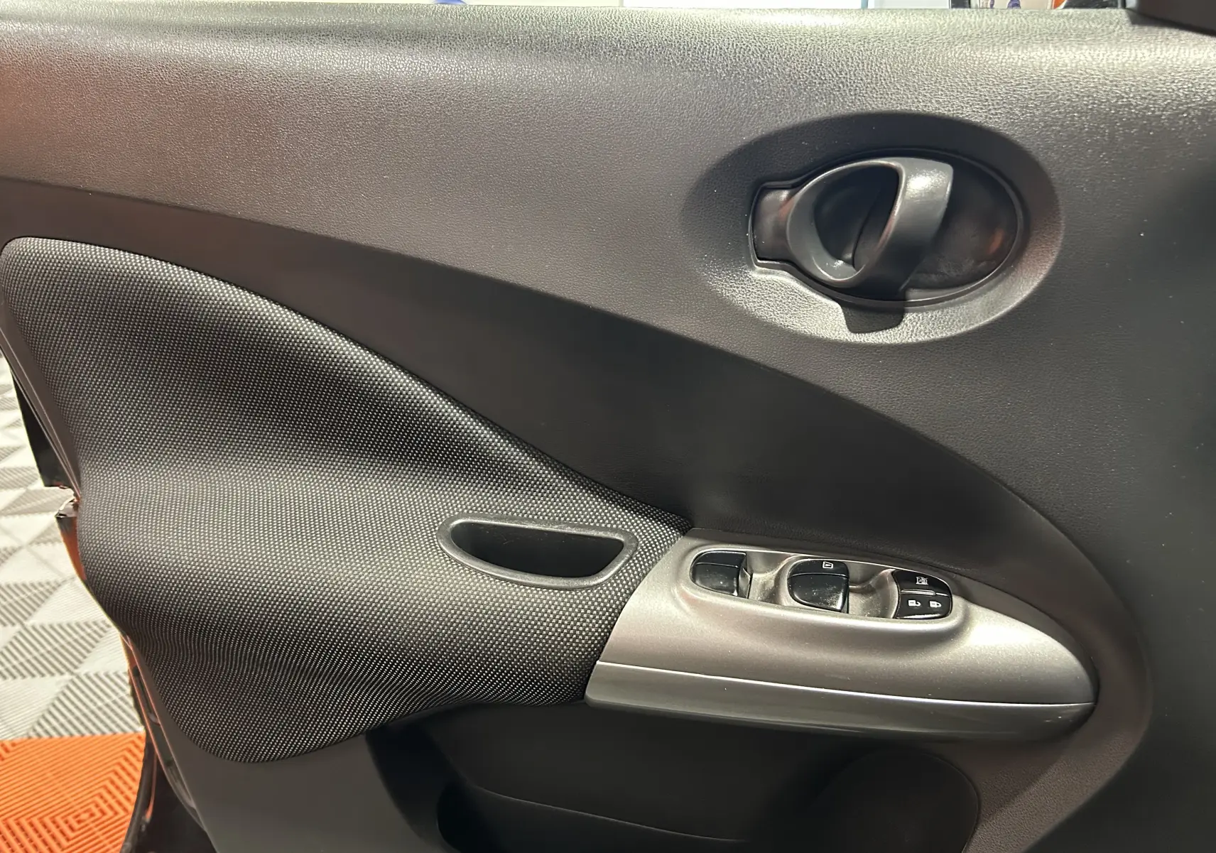 Vue rapprochée de la porte avant gauche du Nissan Juke noir métal, avec commandes de vitres et poignée intérieure.