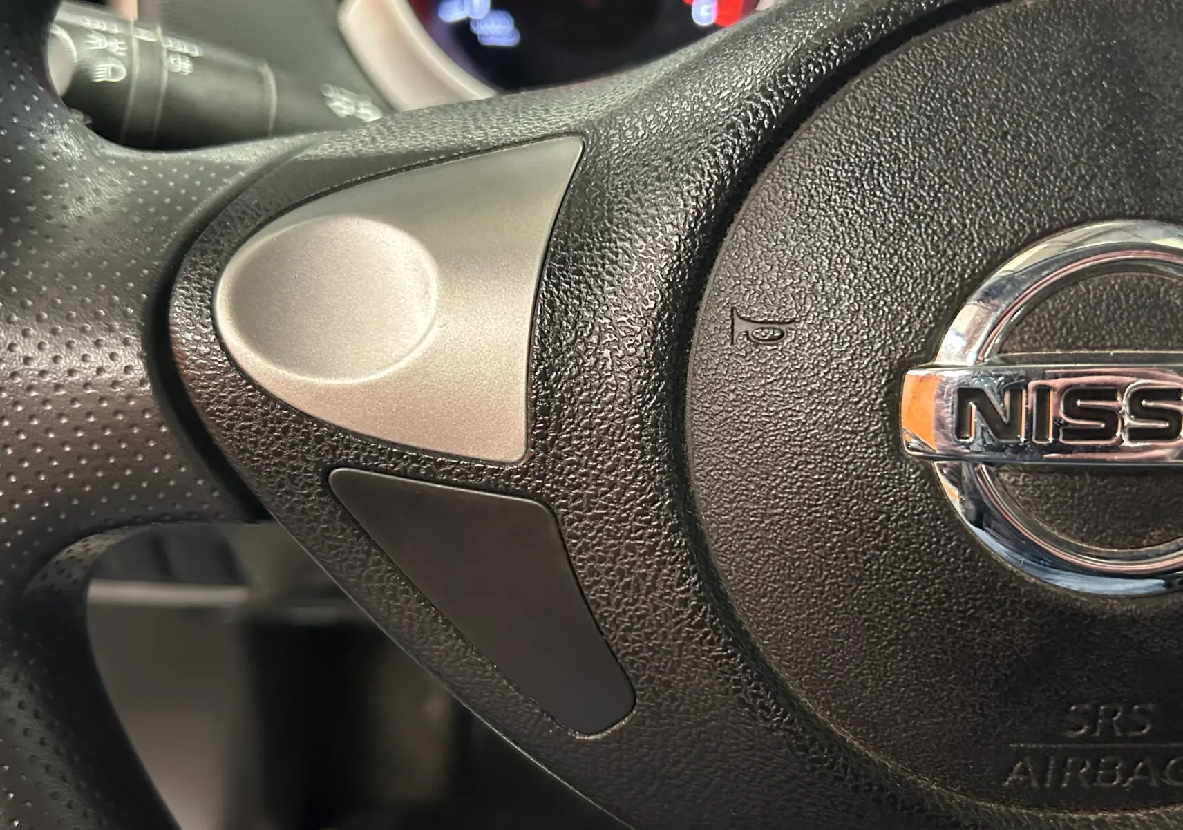 Gros plan sur le volant noir du Nissan Juke 2012, mettant en valeur le logo Nissan chromé au centre.