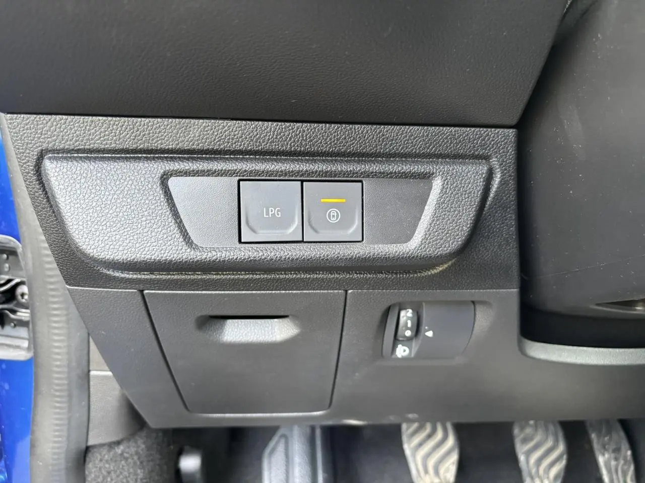 Gros plan sur les commandes LPG et verrouillage sous le tableau de bord côté conducteur d'une Dacia Sandero Bleu Iron.