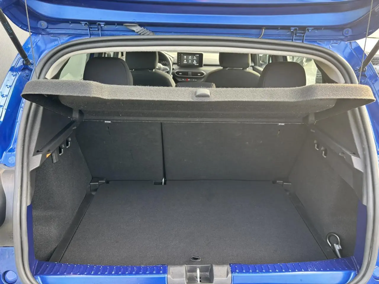 Coffre ouvert vu de l'arrière d'une Dacia Sandero Stepway Bleu Iron, intérieur noir et tablette de coffre relevée.