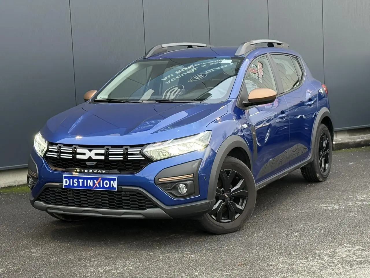 Vue 3/4 avant d'une Dacia Sandero Stepway Bleu Iron avec jantes noires et coques de rétroviseurs cuivrées.