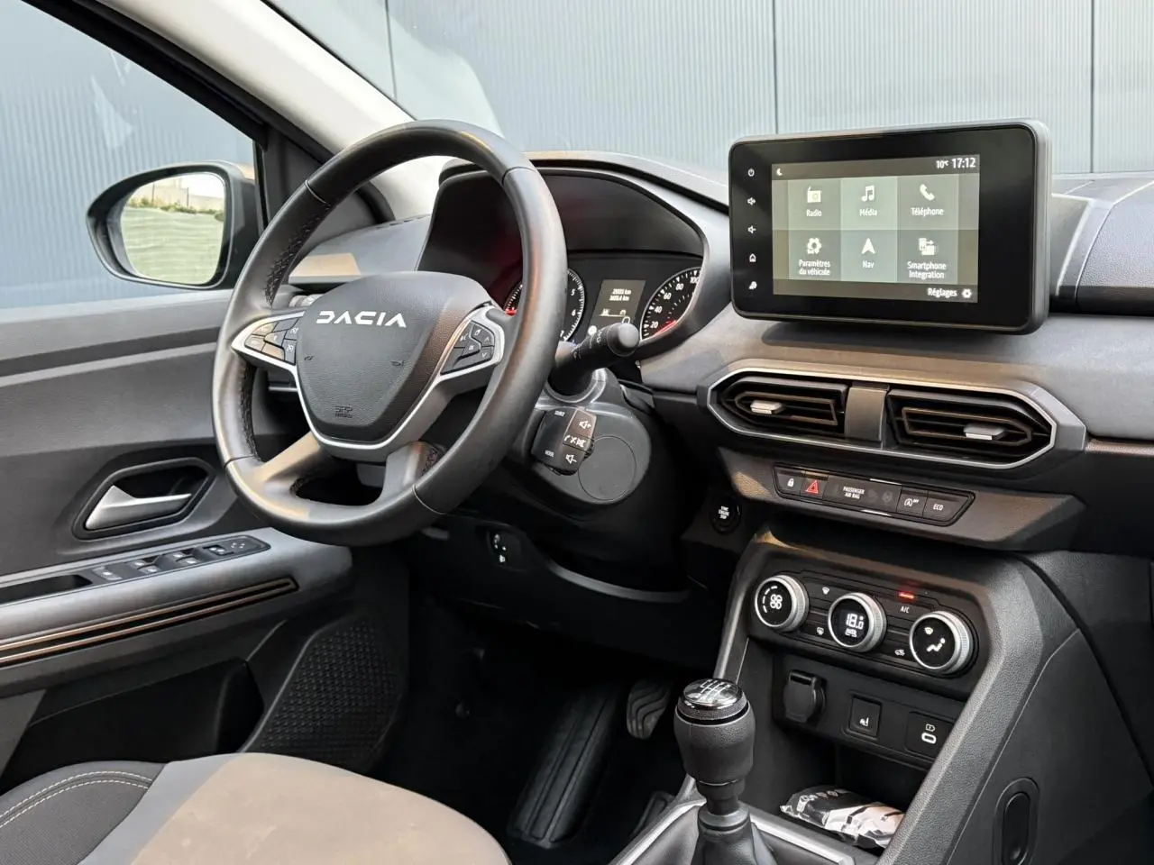 Vue intérieure côté conducteur du tableau de bord et volant Dacia avec écran tactile et commandes au volant.