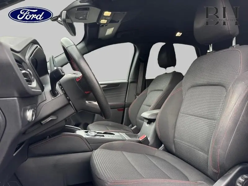Vue intérieure côté conducteur du Ford Kuga 2022, sièges sport noirs avec surpiqûres rouges et volant cuir multifonction.