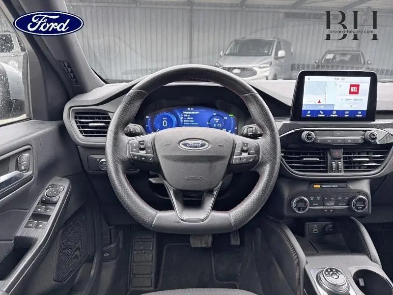 Vue intérieure frontale du tableau de bord et volant cuir multifonction d'un Ford Kuga gris Solar, avec écran tactile et commandes intégrées.