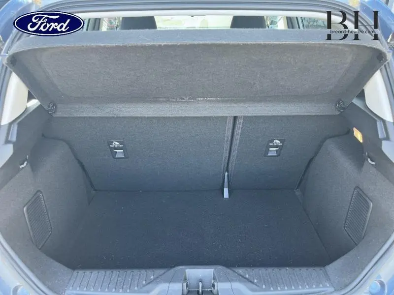 Coffre ouvert vu de l'arrière de la Ford Fiesta 1.0 EcoBoost Hybrid bleu azur, espace de chargement vide et tapis noir.