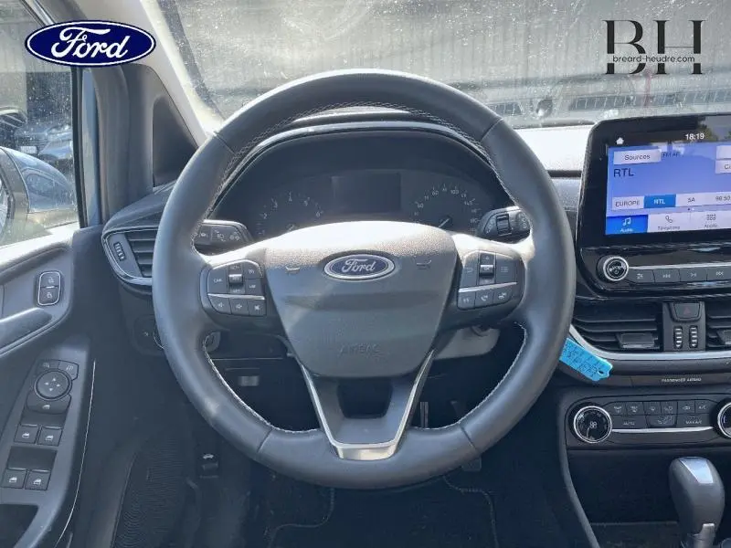 Vue intérieure centrée sur le volant cuir Ford d'une Fiesta 2022 avec écran tactile et commandes au volant.