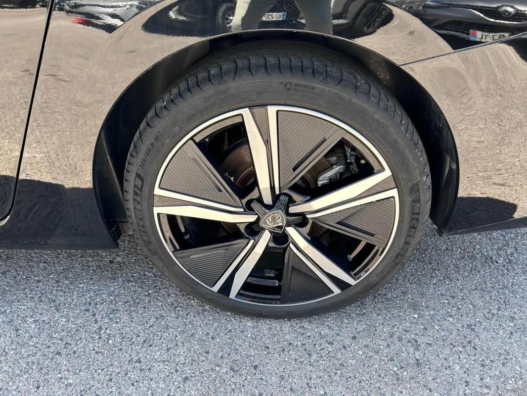 Gros plan sur la jante alliage 18 pouces noire et argentée du côté gauche d'une Peugeot 308 SW PHEV 225 e-EAT8 GT noire.