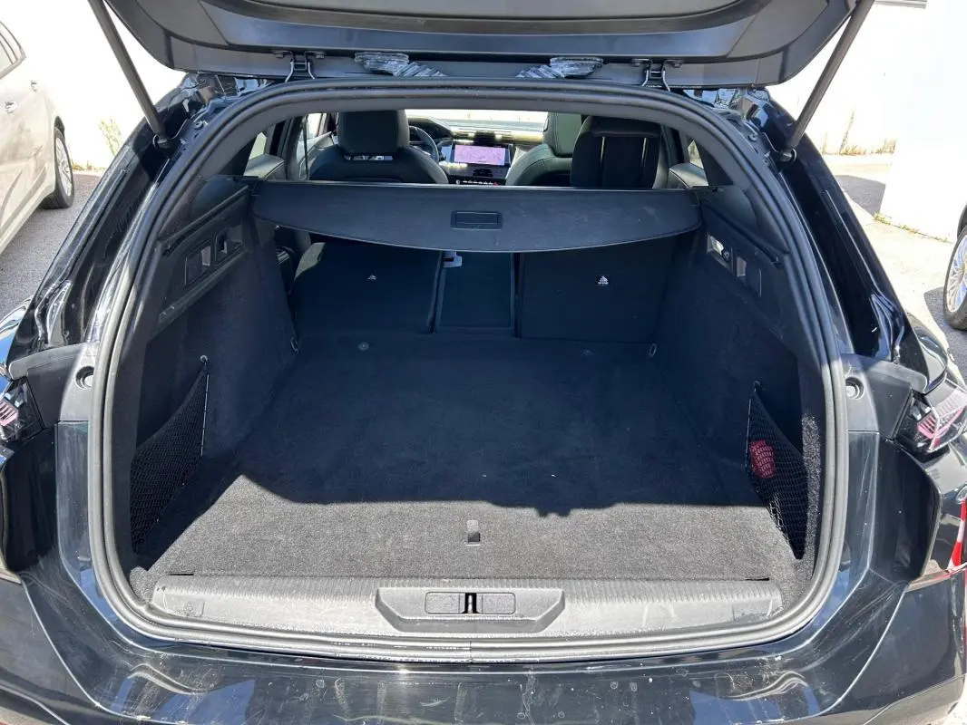 Coffre ouvert vu de l'arrière d'une Peugeot 308 SW PHEV noire, avec banquette arrière rabattable et cache-bagages.
