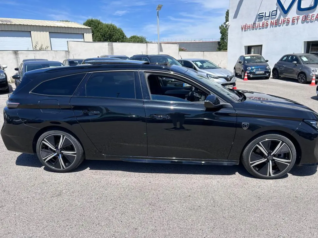 Profil côté gauche d'une Peugeot 308 SW PHEV 225 e-EAT8 GT noire avec jantes alliage 18 pouces et barres de toit.