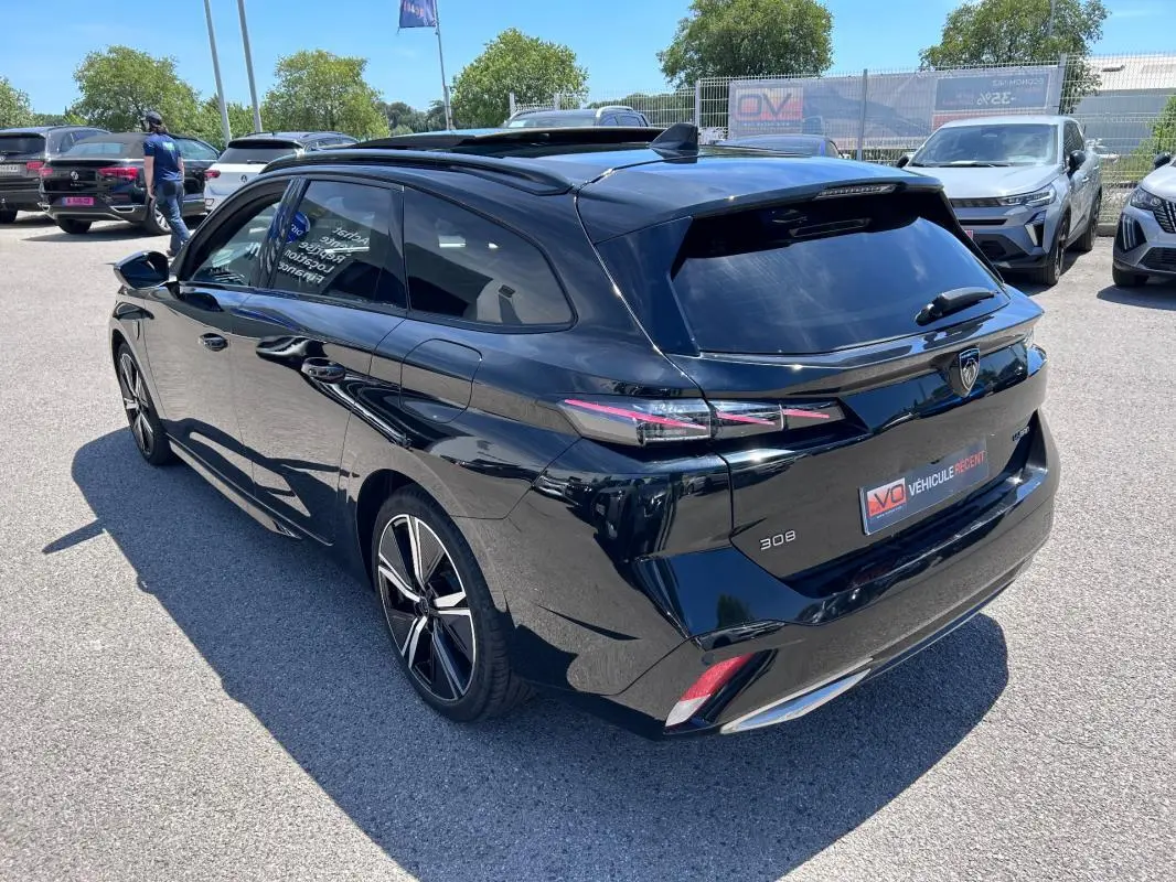 Vue 3/4 arrière droite d'une Peugeot 308 SW PHEV noire 2023 avec jantes alliage 18 pouces et toit ouvrant électrique.