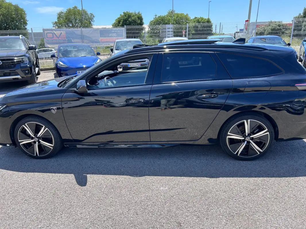 Vue latérale droite d'une Peugeot 308 SW PHEV noire 2023 avec jantes alliage 18 pouces et toit ouvrant électrique.