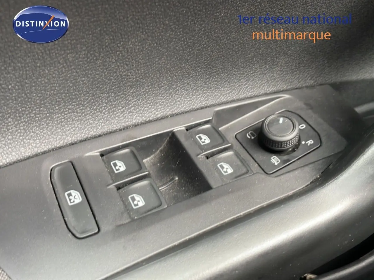 Gros plan sur les commandes de lève-vitres et réglage des rétroviseurs côté conducteur d'une Volkswagen Polo blanche.