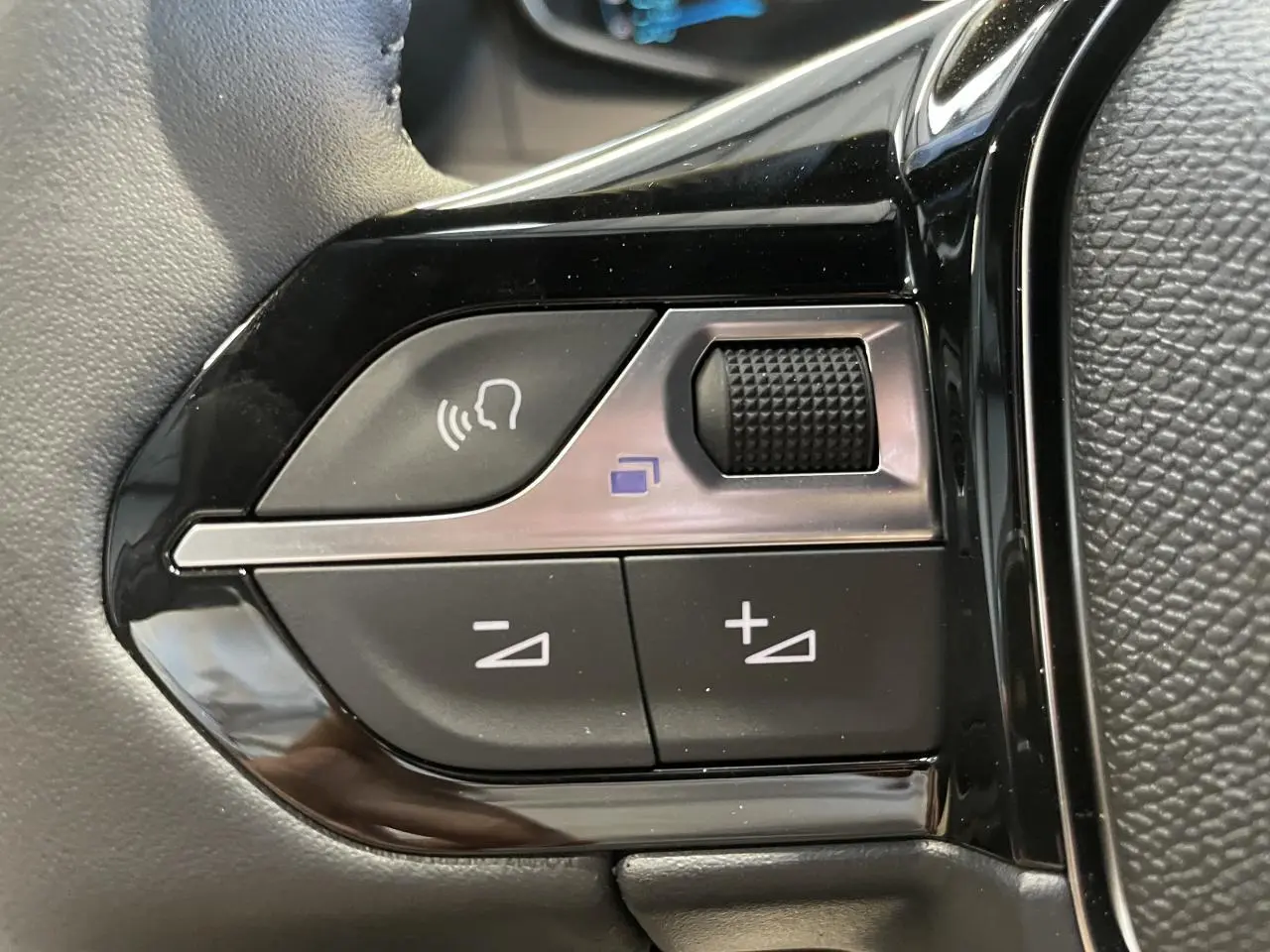 Gros plan sur les commandes de volume et reconnaissance vocale du volant noir du Peugeot 2008 blanc hybride 2026.
