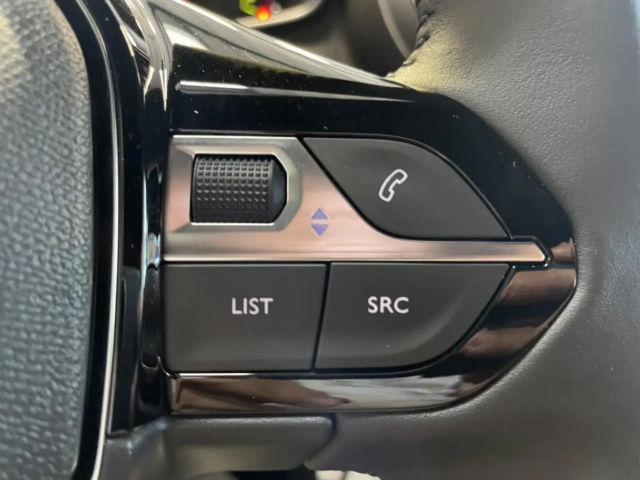 Gros plan sur les commandes multimédia noires intégrées au volant du Peugeot 2008 hybride blanc.