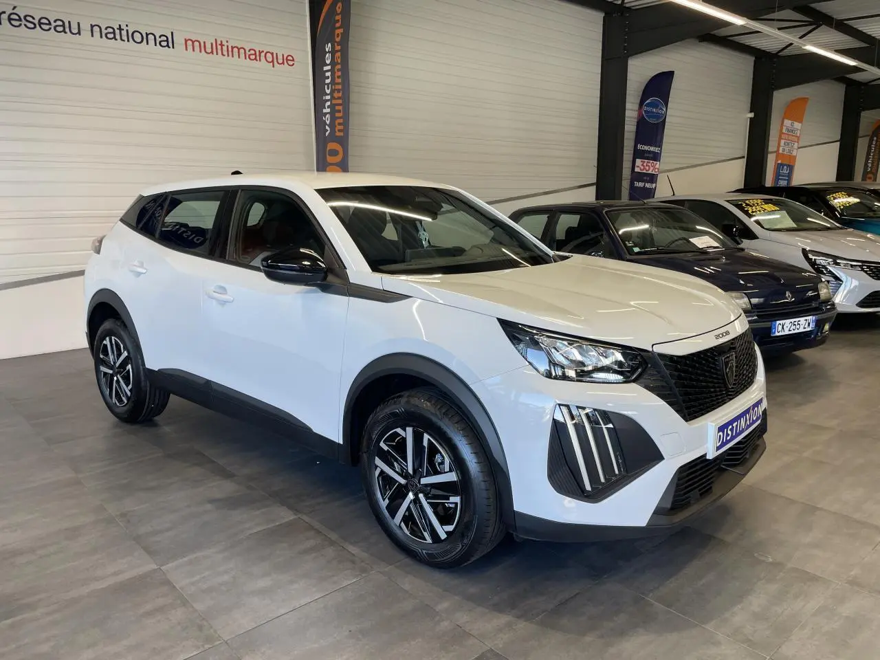 Peugeot 2008 blanc en 3/4 avant droit, avec calandre noire et jantes alliage bicolores, en showroom intérieur.