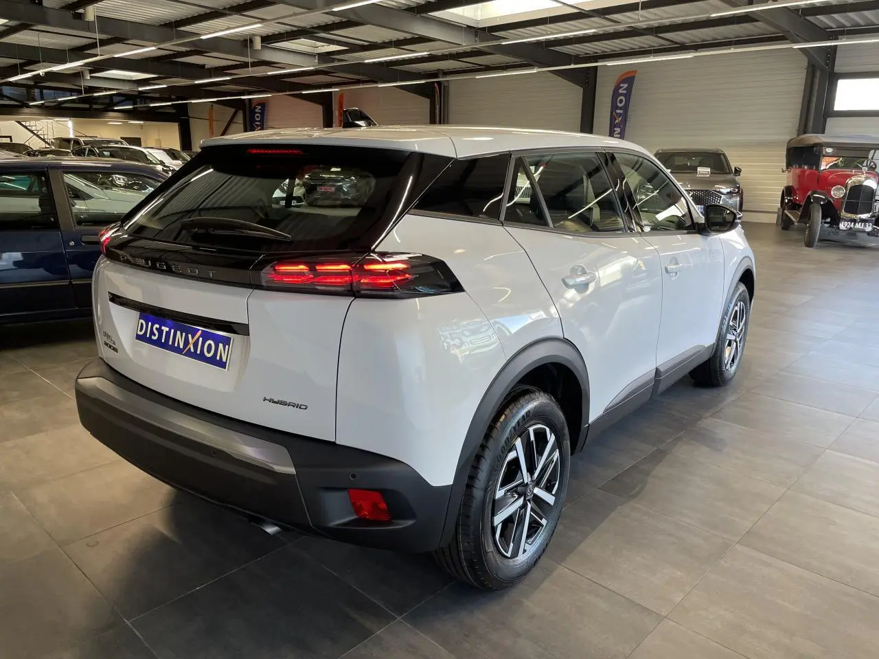 Vue 3/4 arrière droite d’un Peugeot 2008 blanc hybride en showroom avec feux arrière LED allumés et jantes alliage.