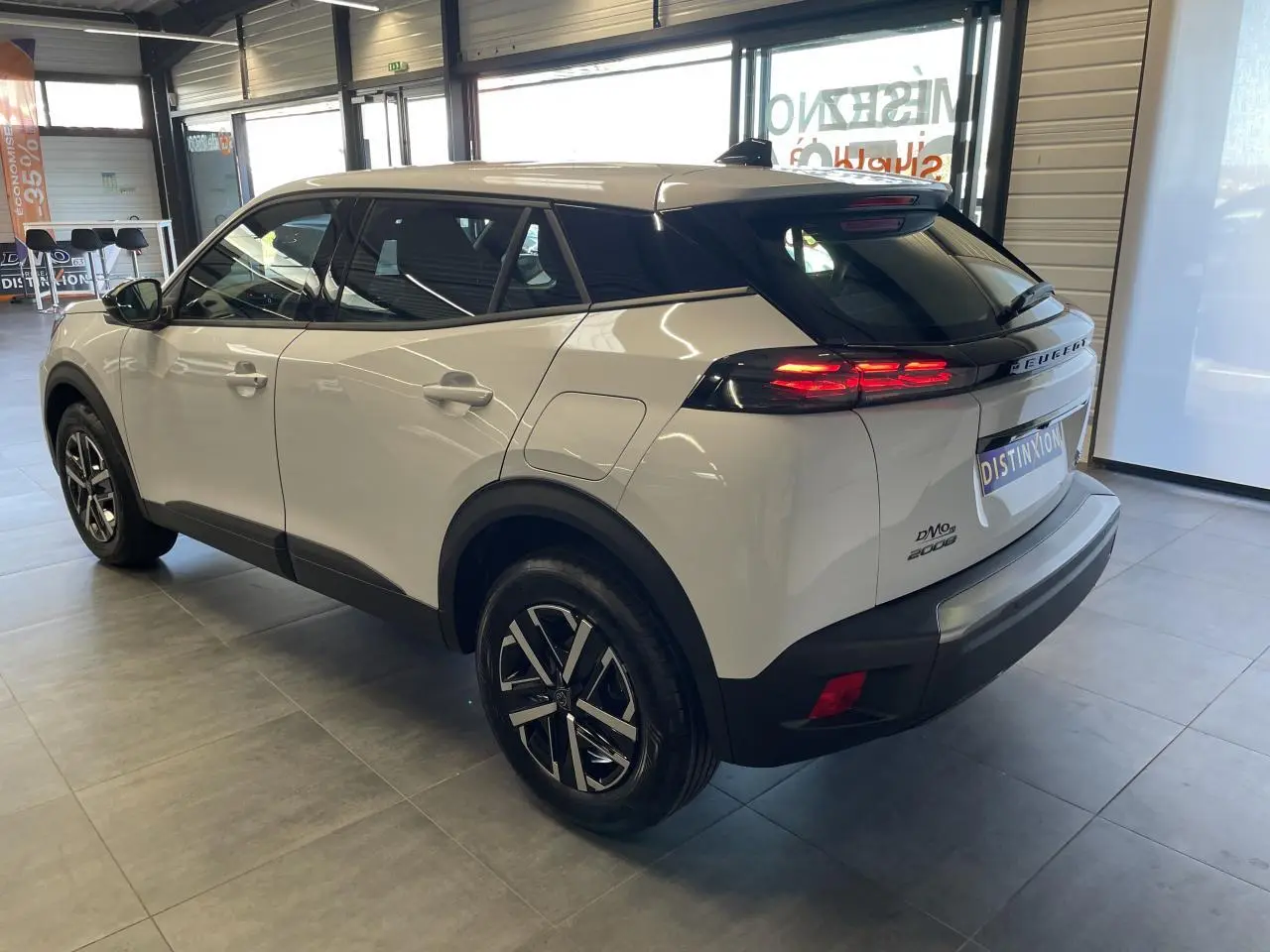Peugeot 2008 blanc vue 3/4 arrière droit en intérieur, feux arrière LED allumés et jantes alliage noires.