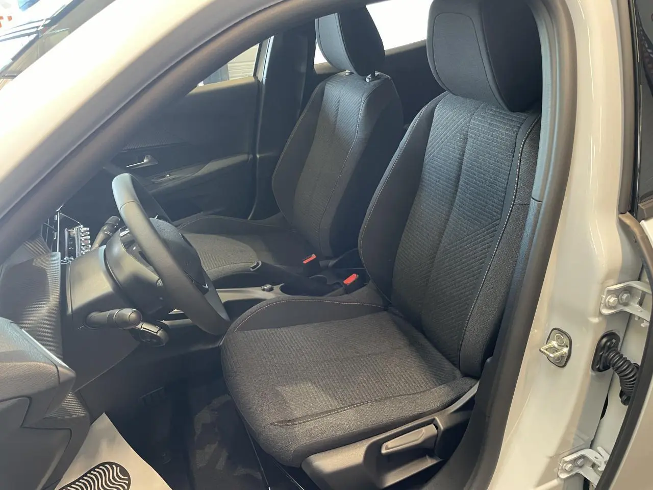 Vue intérieure côté conducteur du Peugeot 2008 blanc, mettant en valeur les sièges tissu gris et le volant compact noir.