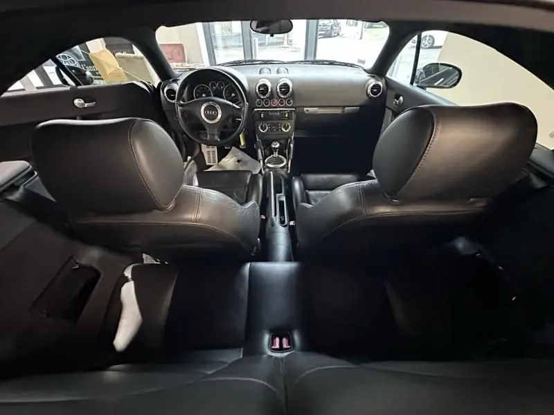 Intérieur noir de l'Audi TT Coupé 2002, vue depuis l'arrière montrant le tableau de bord et la boîte manuelle.