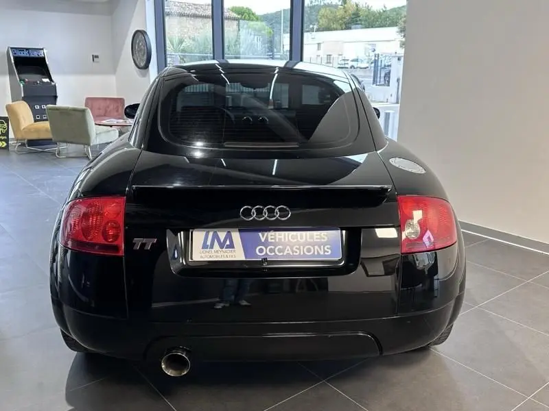 Vue arrière d'une Audi TT Coupé noire de 2002, avec feux rouges et logo TT visible, en intérieur showroom.