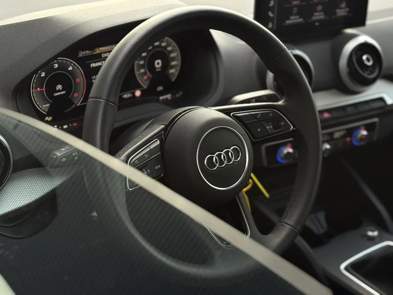 Vue intérieure rapprochée du volant cuir multifonction de l’Audi Q2 30 TDI S-Line avec tableau de bord numérique.