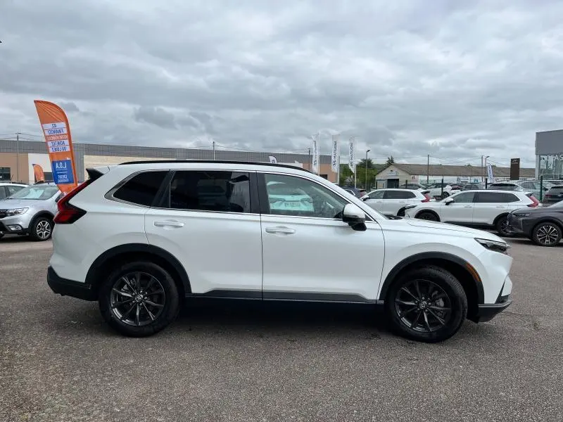 Vue de profil côté gauche d'un Honda CR-V 2024 blanc platine nacré avec jantes alliage noires sur parking.
