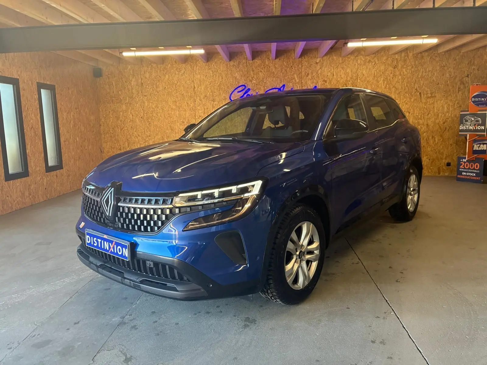 Renault Austral bleu en 3/4 avant droit dans un showroom, avec calandre distinctive et phares LED allumés.