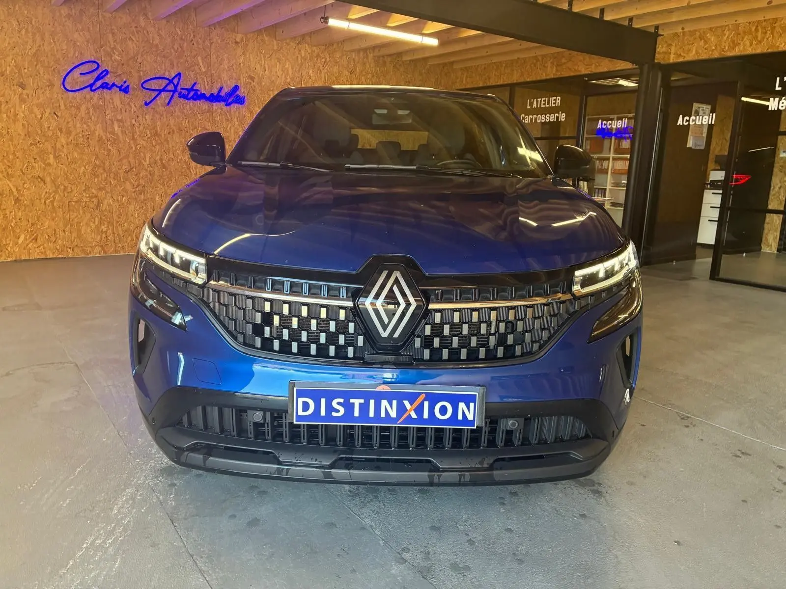 Vue de face d'un Renault Austral bleu 2024 avec calandre à damier et logo central, dans un showroom intérieur.