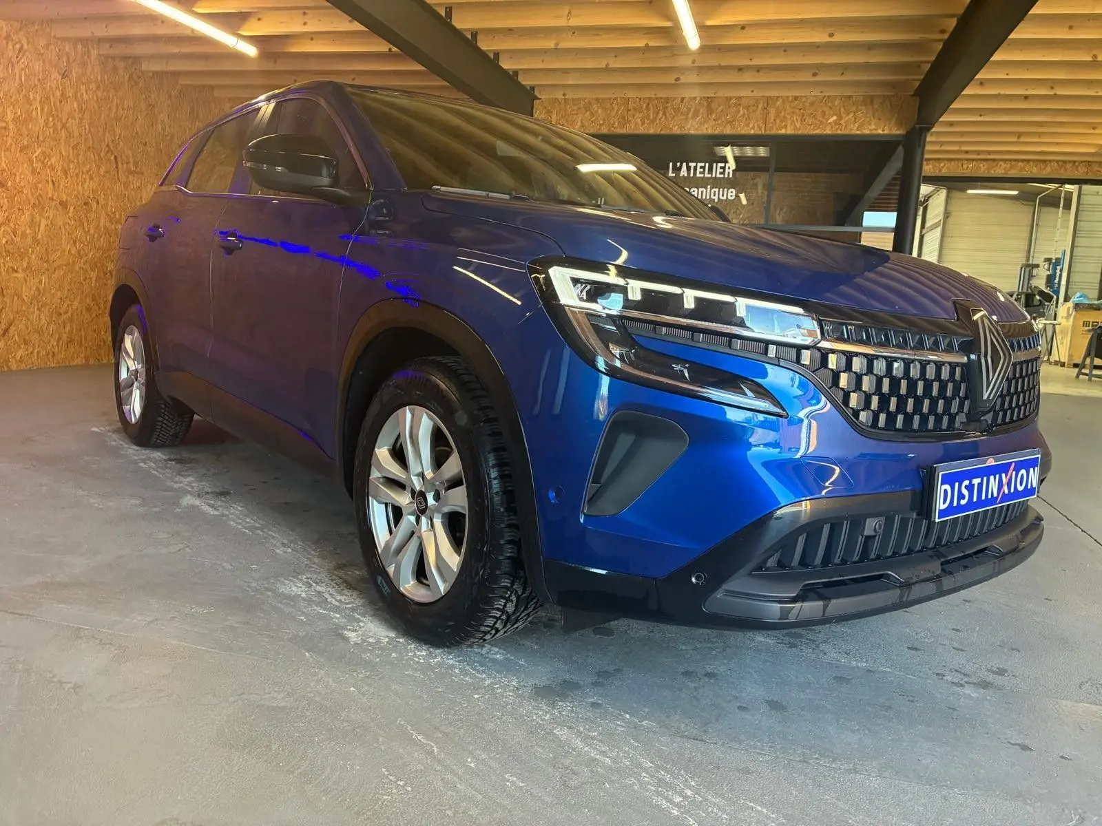 Renault Austral bleu en 3/4 avant droit dans un garage, mettant en valeur sa calandre et ses phares LED modernes.