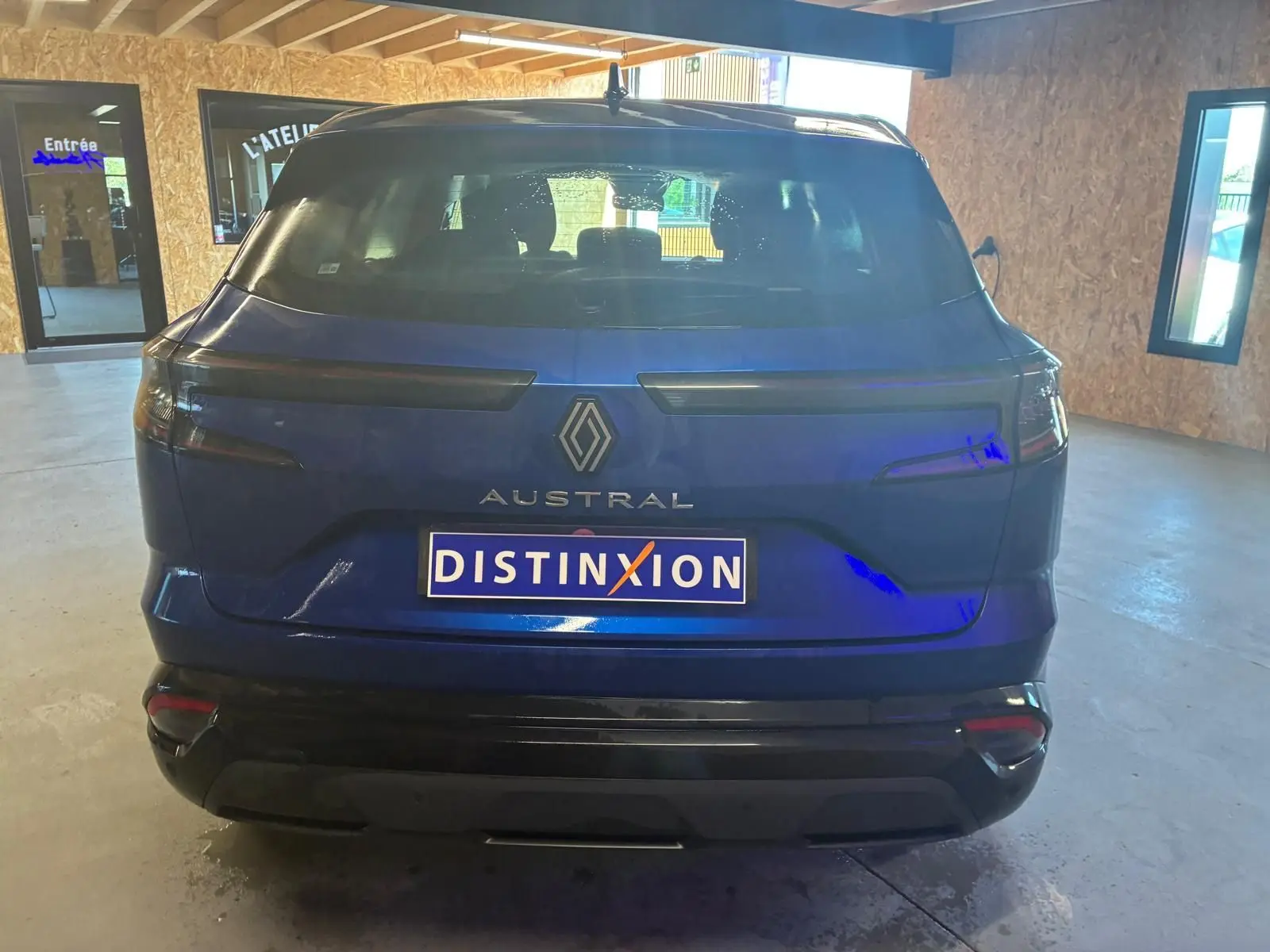 Vue arrière d'un Renault Austral bleu 2024 avec feux arrière étirés et plaque Distinxion visible en intérieur.