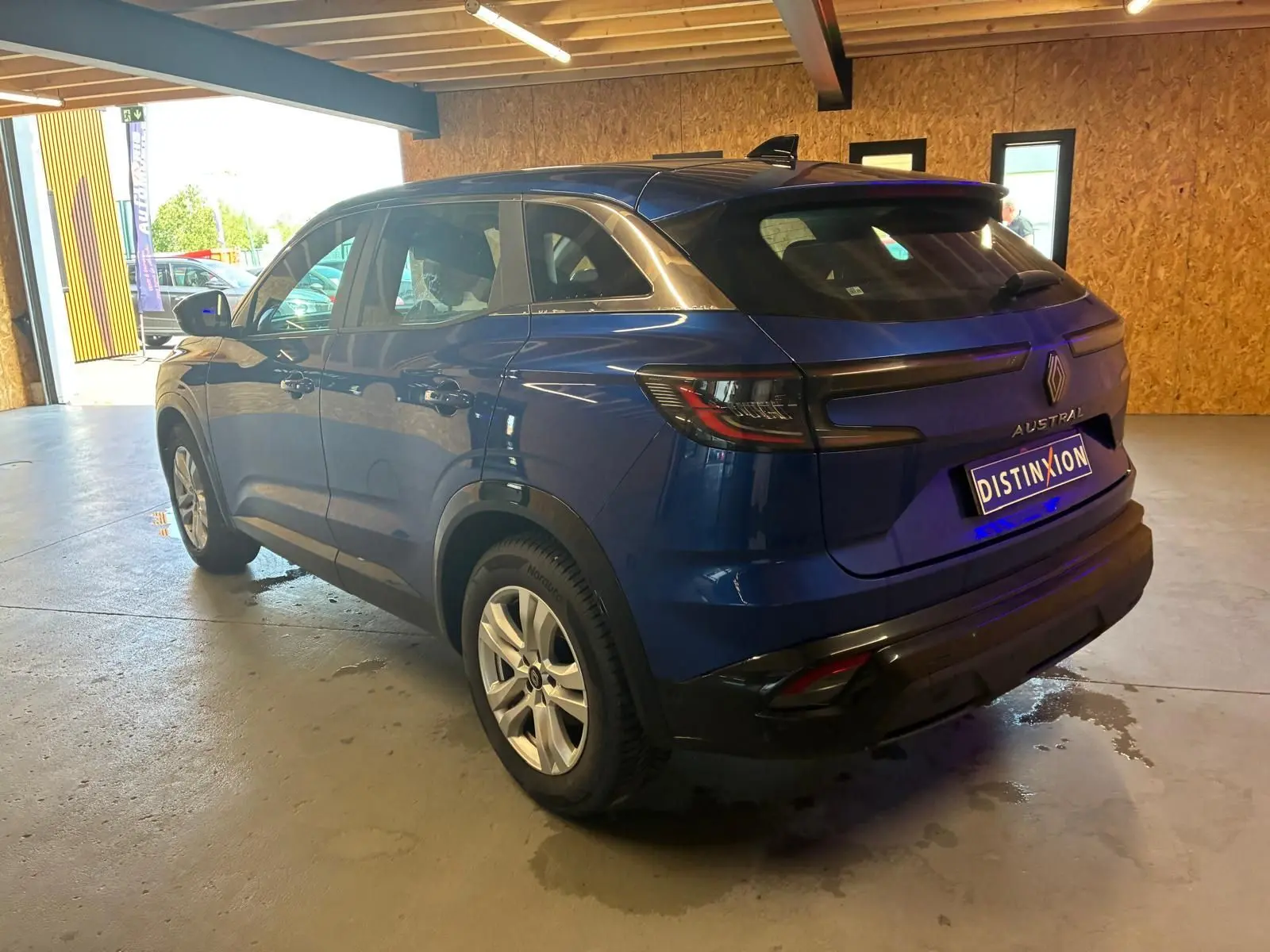 Vue 3/4 arrière droite d'un Renault Austral bleu 2024 avec feux arrière LED et toit noir dans un garage.