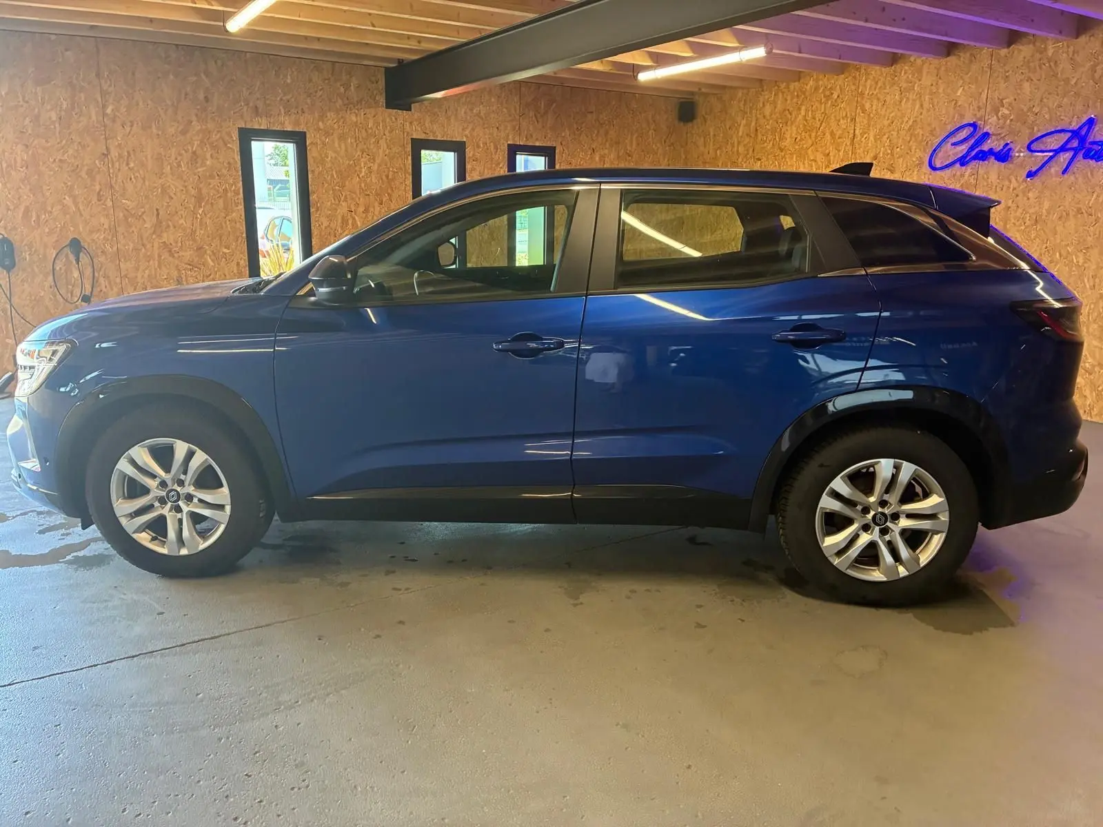 Profil droit d’un Renault Austral bleu 2024 stationné en intérieur, avec jantes argentées et toit noir contrastant.