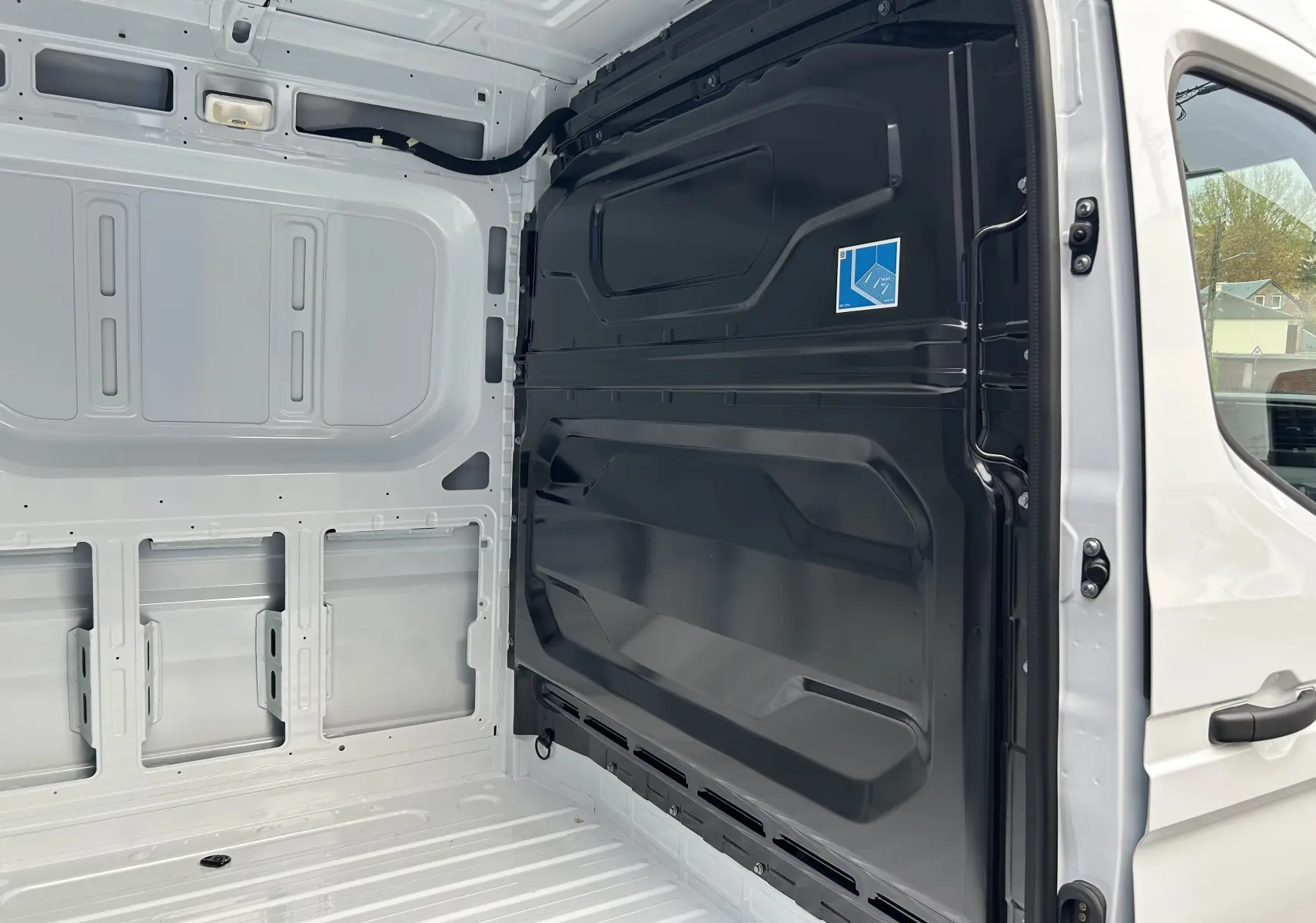 Intérieur du fourgon Renault Master blanc vu de l’arrière droit, montrant la cloison noire séparatrice et la paroi blanche.