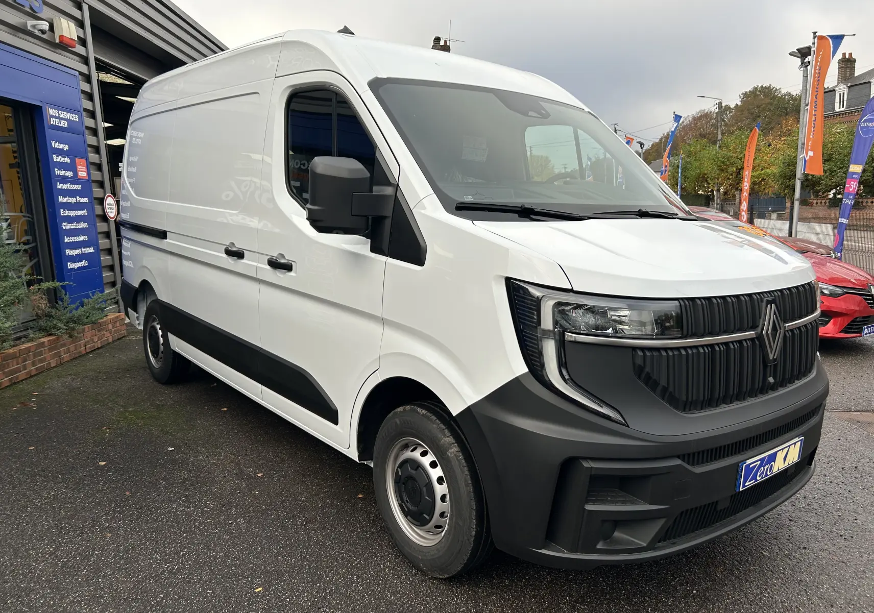 Renault Master blanc vu en 3/4 avant droit, avec calandre noire et roues acier, stationné devant un atelier.