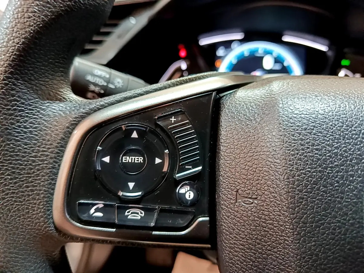 Gros plan sur les commandes du volant cuir côté gauche de la Honda Civic 2020 gris foncé avec tableau de bord éclairé.