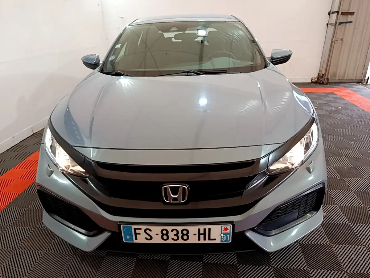 Vue avant d'une Honda Civic 1.0 i-VTEC Exclusive gris foncé, phares allumés dans un garage.