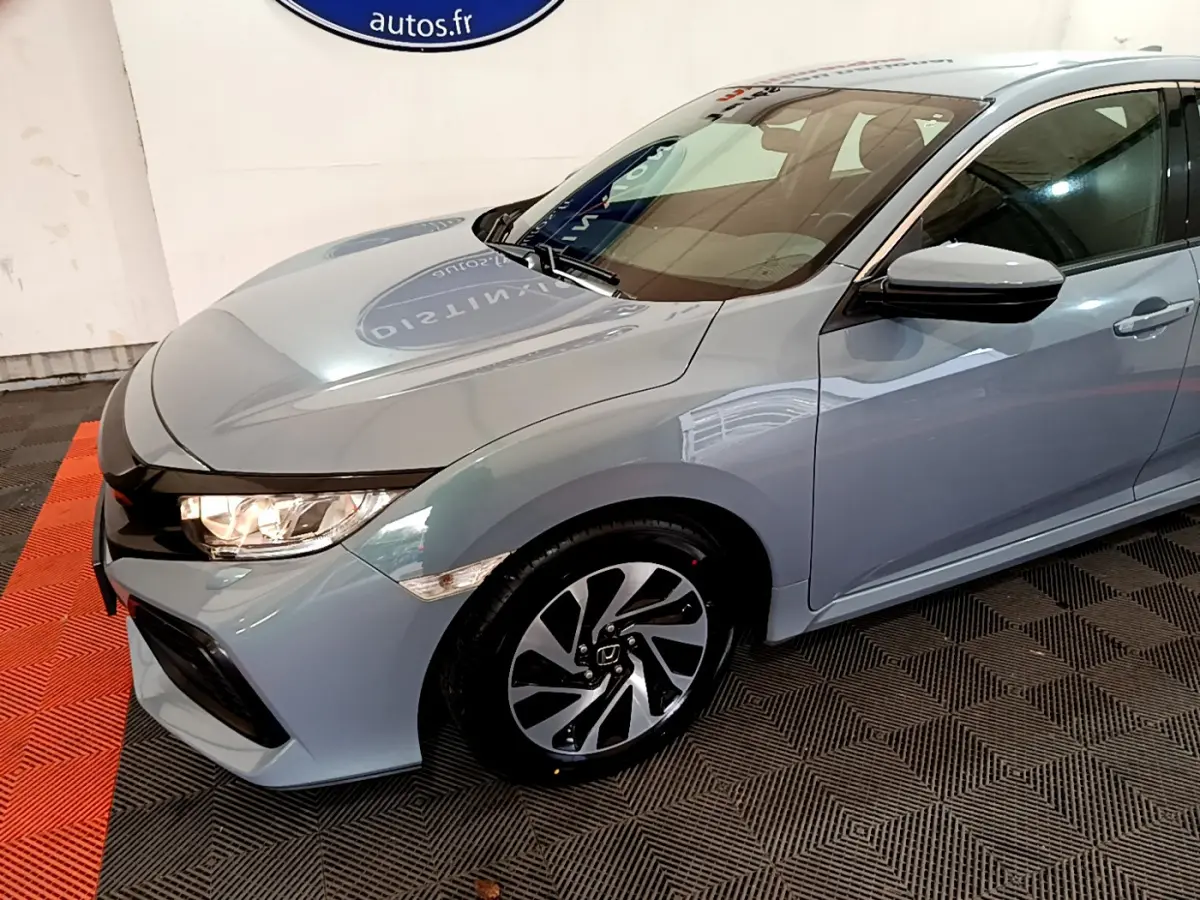 Vue 3/4 avant droit d'une Honda Civic gris clair avec jantes alliage et phares allumés en intérieur showroom.