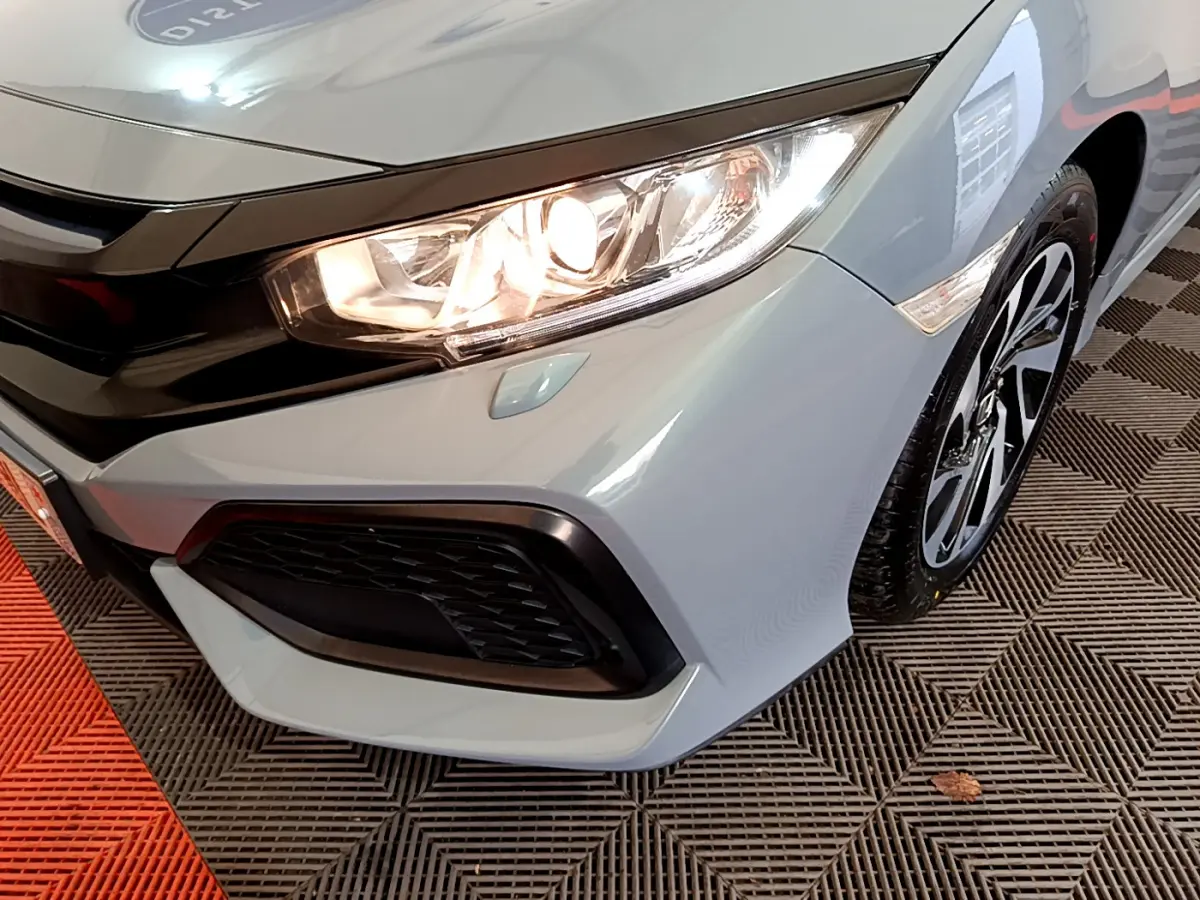Gros plan sur l'avant droit gris clair de la Honda Civic 1.0 i-VTEC avec phare allumé et jante alliage noire.