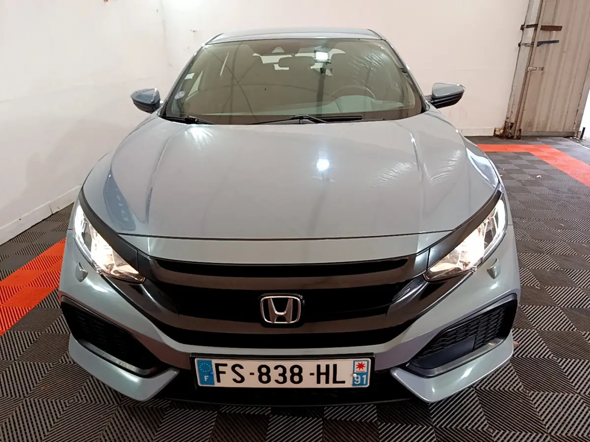 Vue frontale d'une Honda Civic 1.0 i-VTEC Exclusive gris foncé avec phares allumés en intérieur.