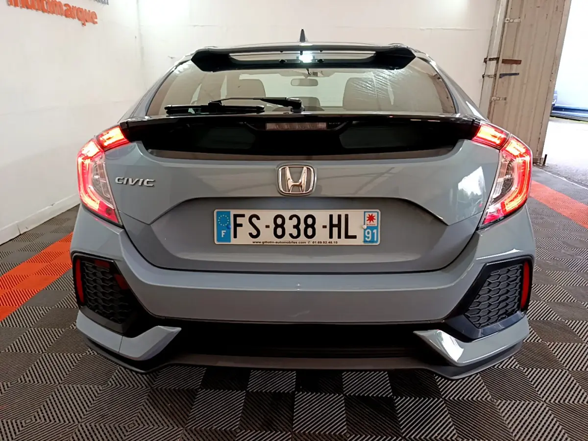 Vue arrière d'une Honda Civic gris foncé 2020 avec feux arrière allumés et aileron noir.