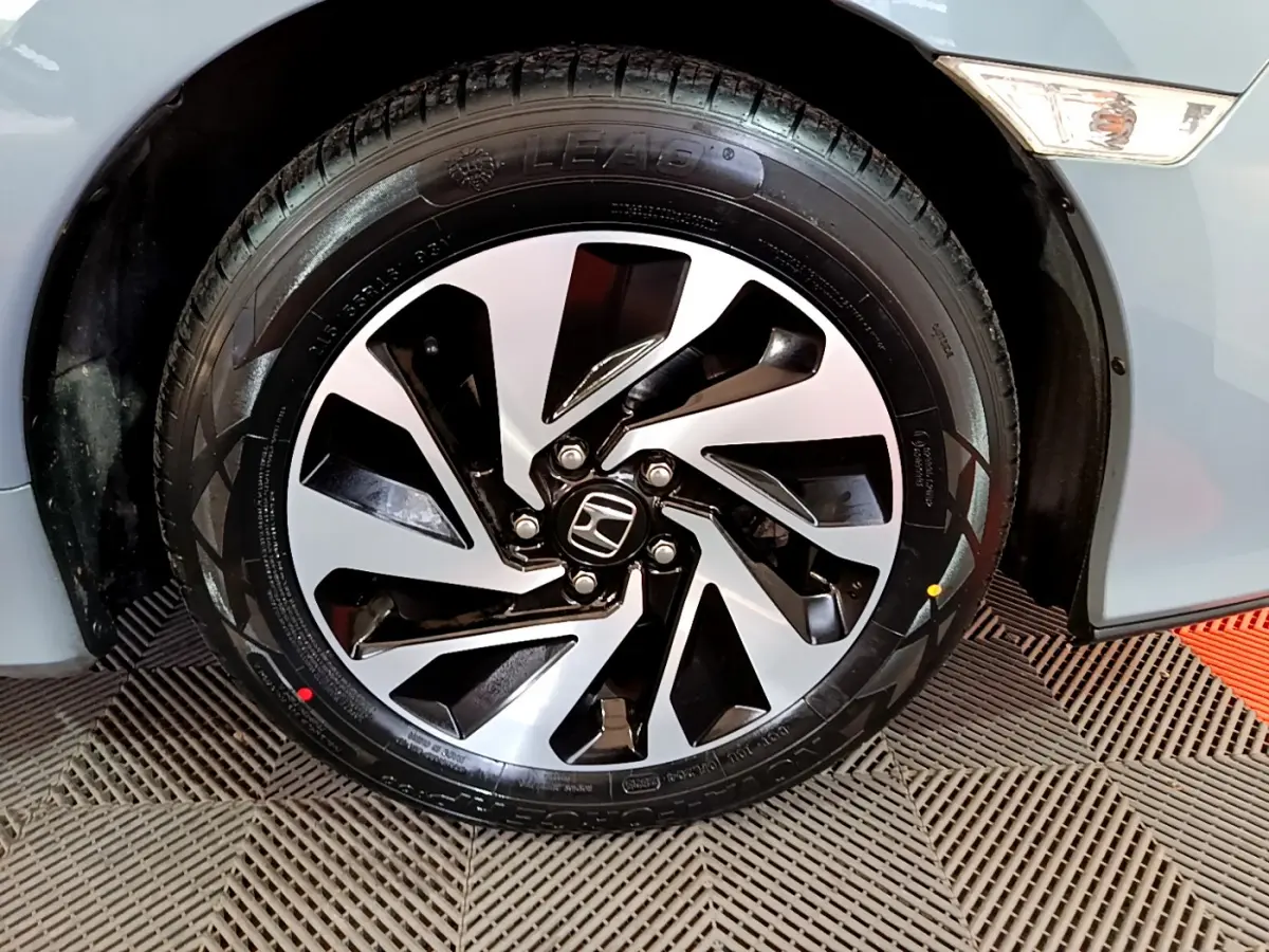 Gros plan sur la roue avant gauche d'une Honda Civic 1.0 i-VTEC Exclusive gris foncé avec jante alliage noire et argentée.