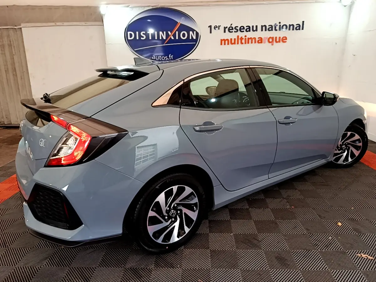 Vue 3/4 arrière droite d'une Honda Civic 1.0 i-VTEC Exclusive gris foncé avec feux arrière allumés et jantes stylisées.