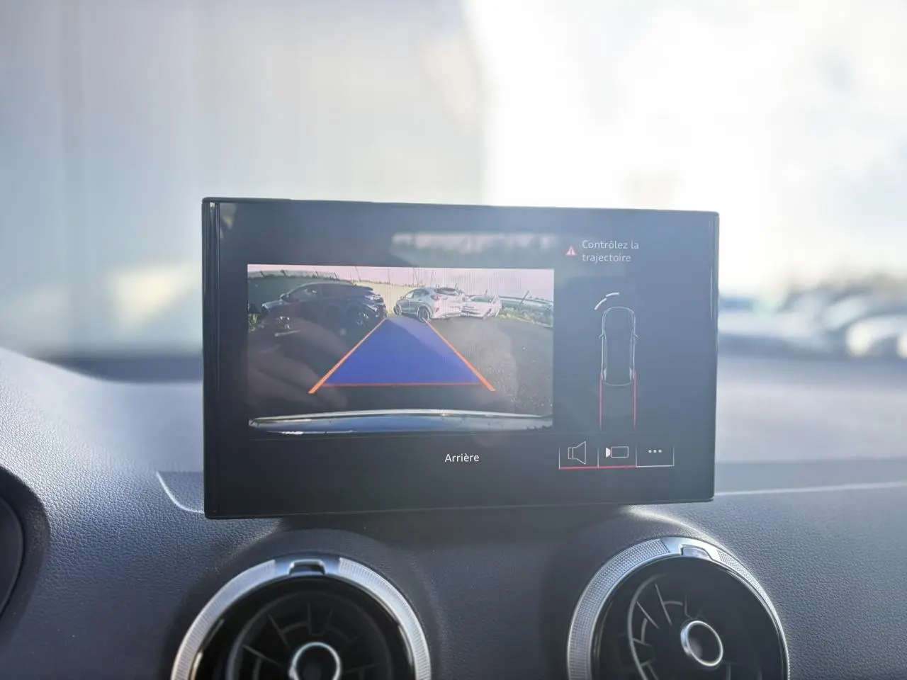 Écran central affichant la caméra de recul avec guidage dynamique dans un Audi Q2 gris Daytona, vue intérieure avant.