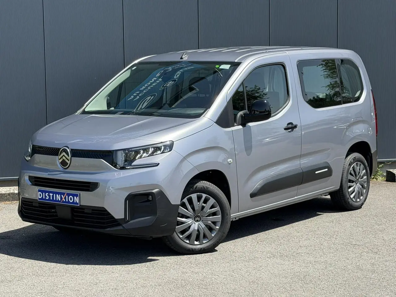 Citroën Berlingo ë-136 gris Artense en 3/4 avant droit, avec jantes tôles et protections latérales noires.